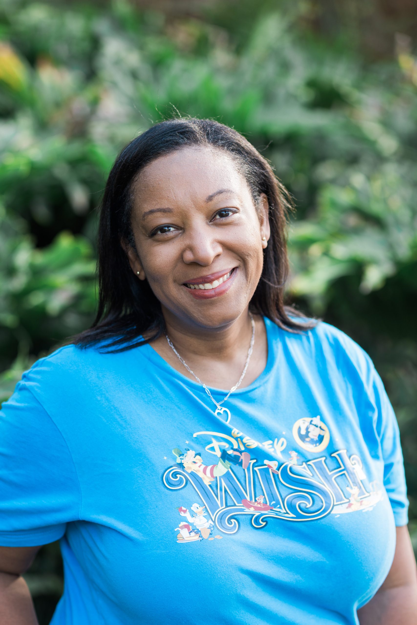 Smiling woman wearing a blue Disney Wish t-shirt, surrounded by lush greenery, representing personalized travel experiences with Once Upon A Trip Travel.